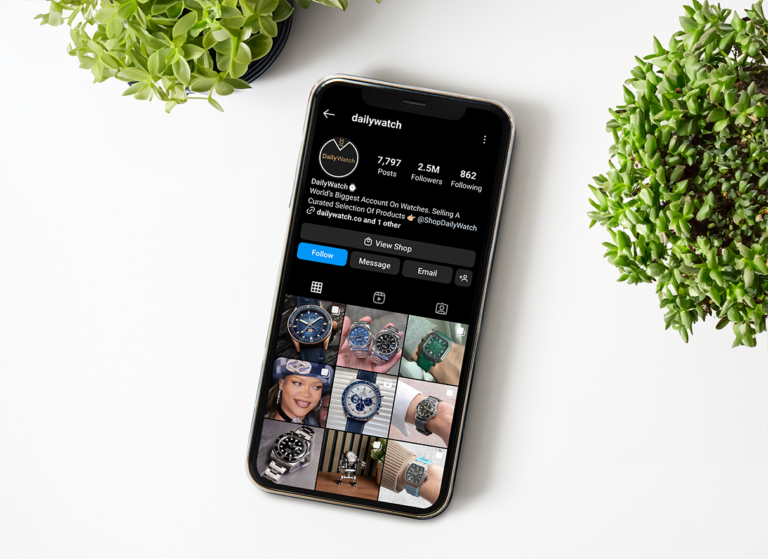 telefon på hvid bordplade med planter, der viser Instagram-kanalen DailyWatch